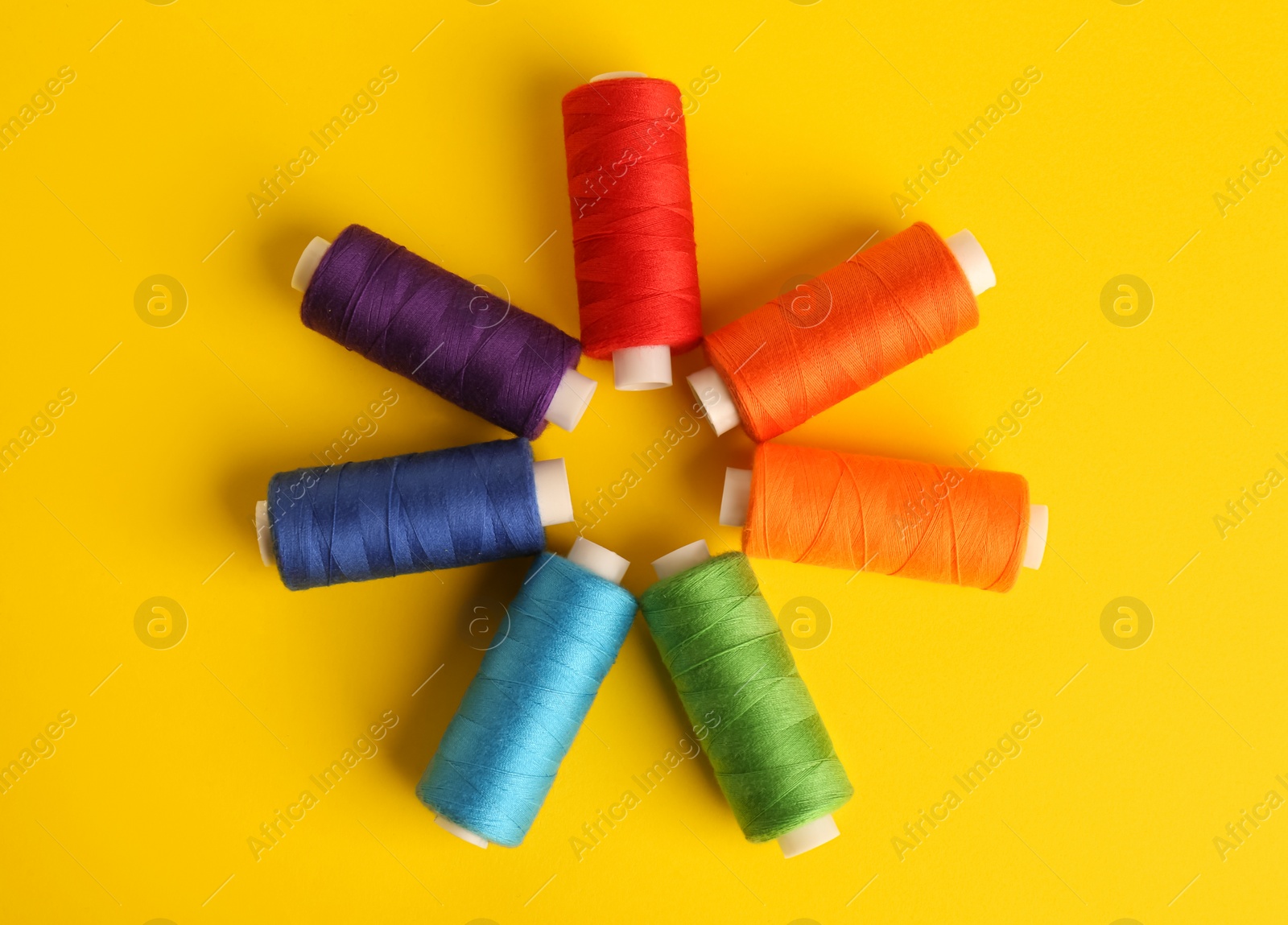 Photo of Different colorful sewing threads on yellow background, flat lay