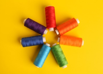Photo of Different colorful sewing threads on yellow background, flat lay