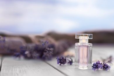 Photo of Bottle of luxury perfume and lavender flowers on white wooden table outdoors. Space for text