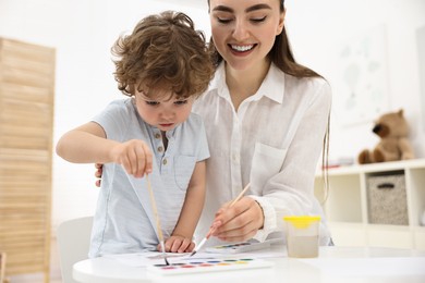 Photo of Mother and her little son painting with watercolor at home, closeup