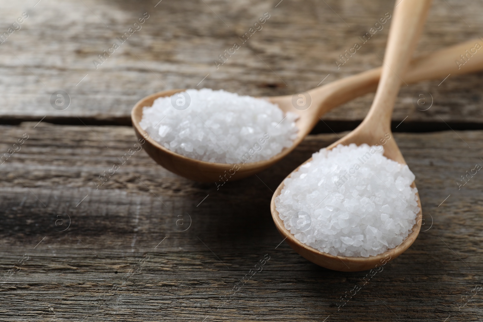 Photo of Organic salt in spoons on wooden table, closeup