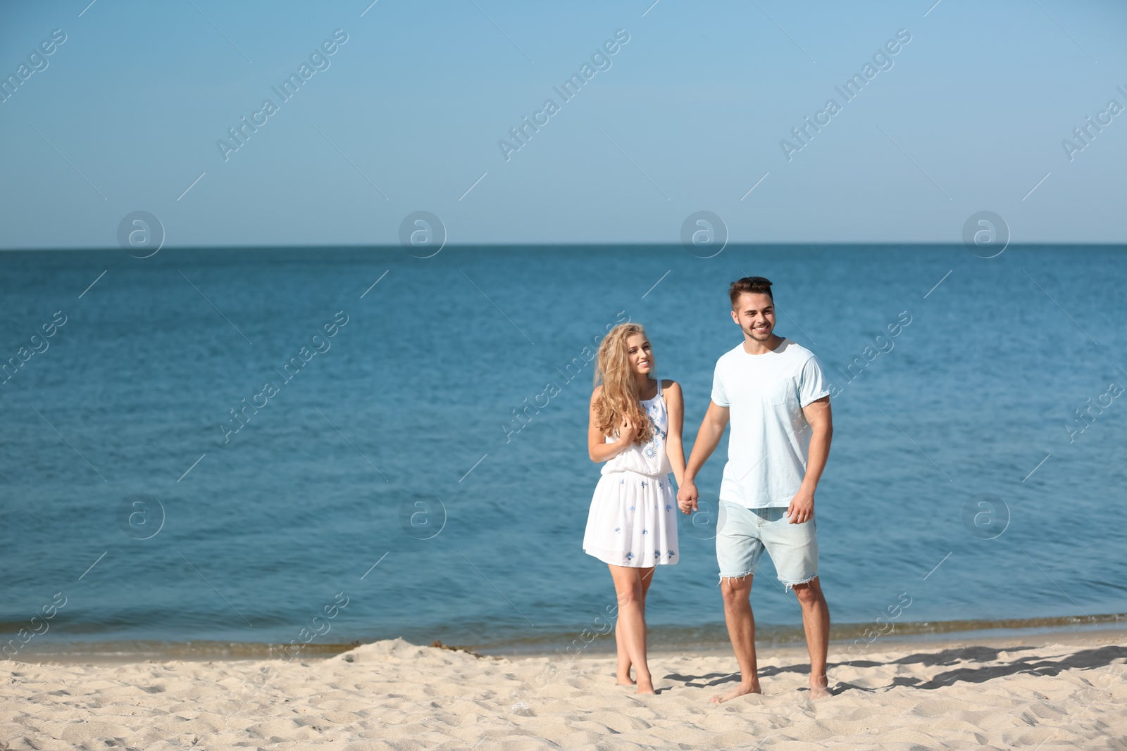 Photo of Happy young couple holding hands at beach on sunny day