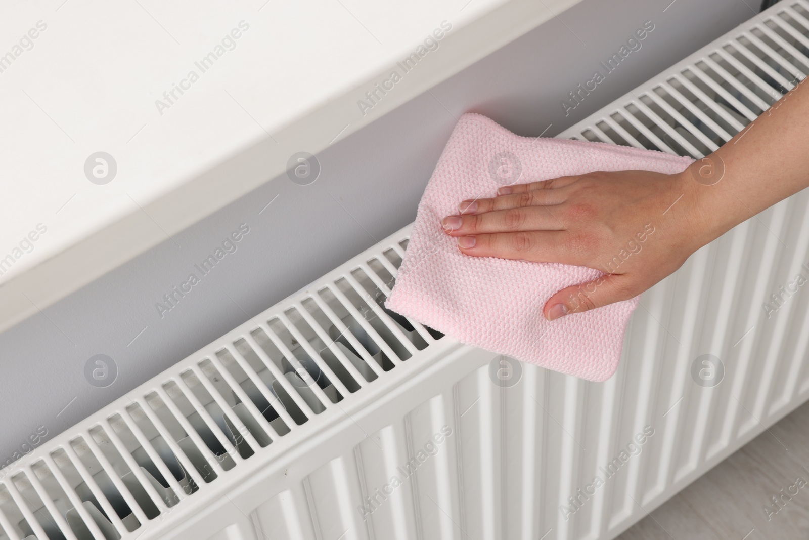 Photo of Woman cleaning white radiator with rag indoors, above view