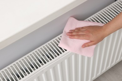 Photo of Woman cleaning white radiator with rag indoors, above view