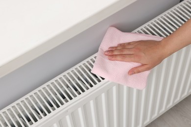 Woman cleaning white radiator with rag indoors, above view