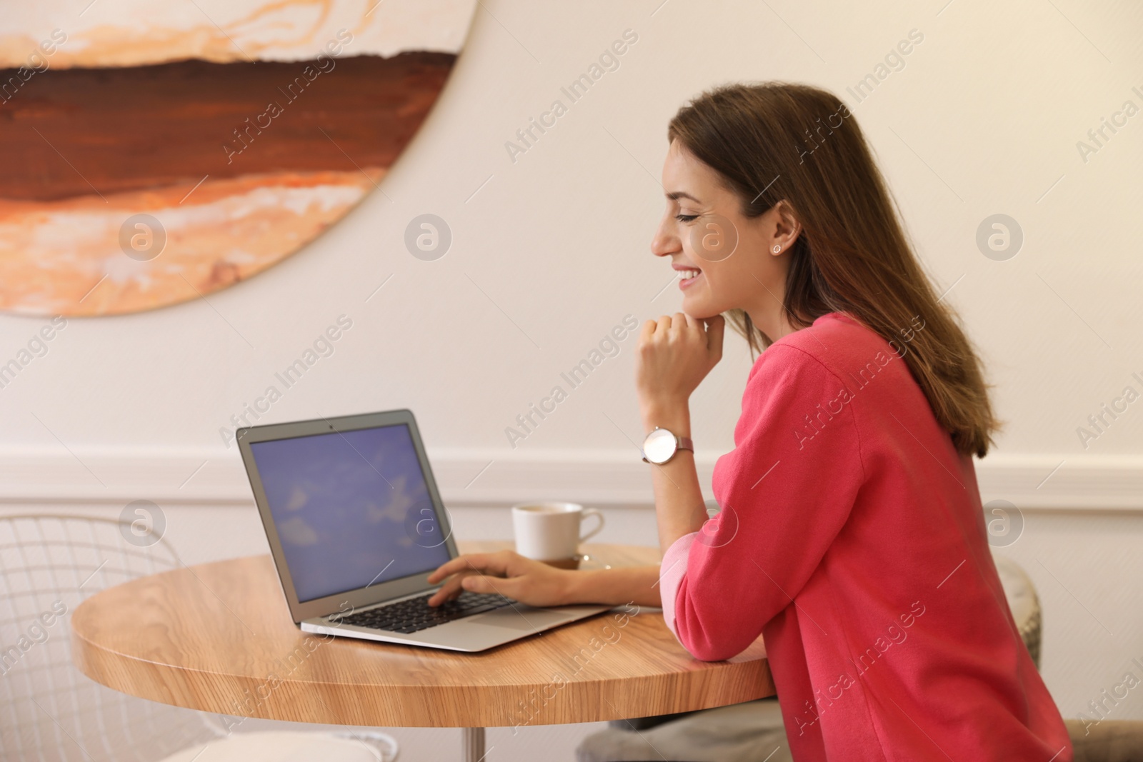 Photo of Young blogger working with laptop at table in cafe