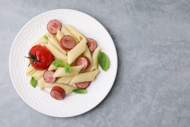 Tasty pasta with smoked sausage, tomato and basil on light grey table, top view. Space for text