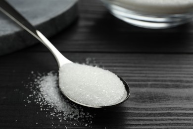 Photo of Spoon with granulated sugar on black wooden table, closeup