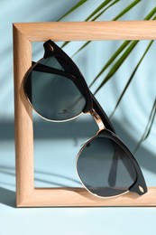 Photo of Stylish sunglasses near photo frame on light blue background