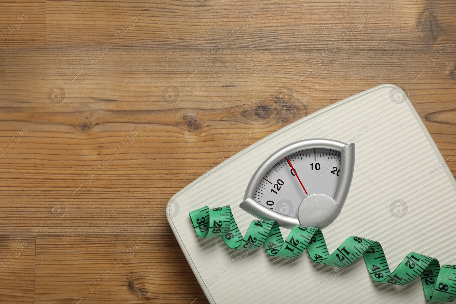 Photo of Scales and measuring tape on wooden floor, top view. Space for text