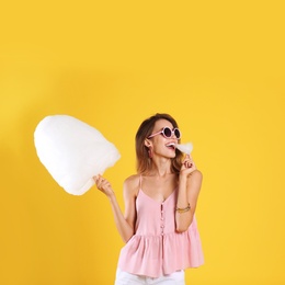 Photo of Happy young woman eating cotton candy on yellow background