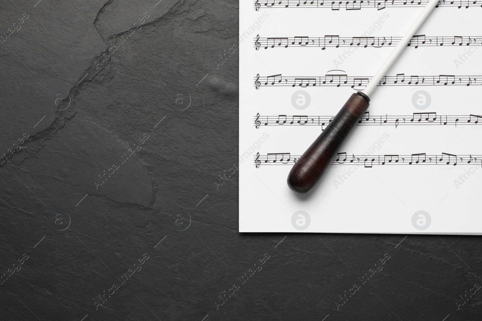 Photo of Conductor's baton and sheet music on black background, top view. Space for text