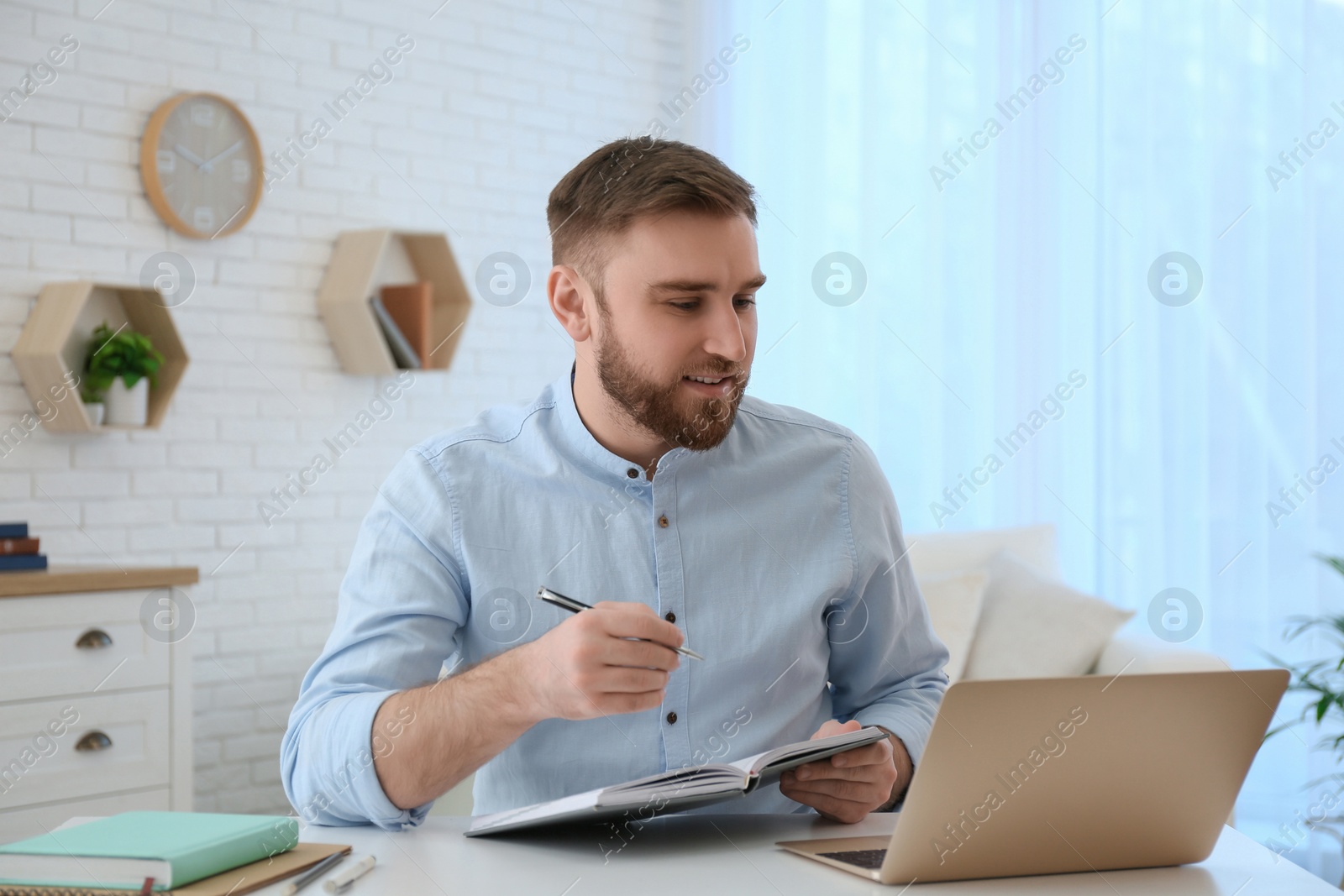 Photo of Young man taking notes during online webinar at table indoors