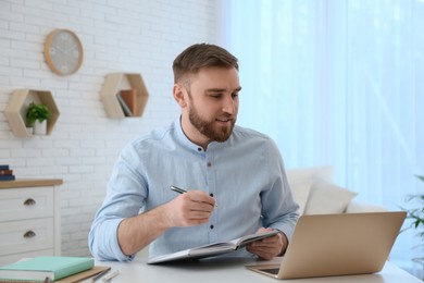 Photo of Young man taking notes during online webinar at table indoors