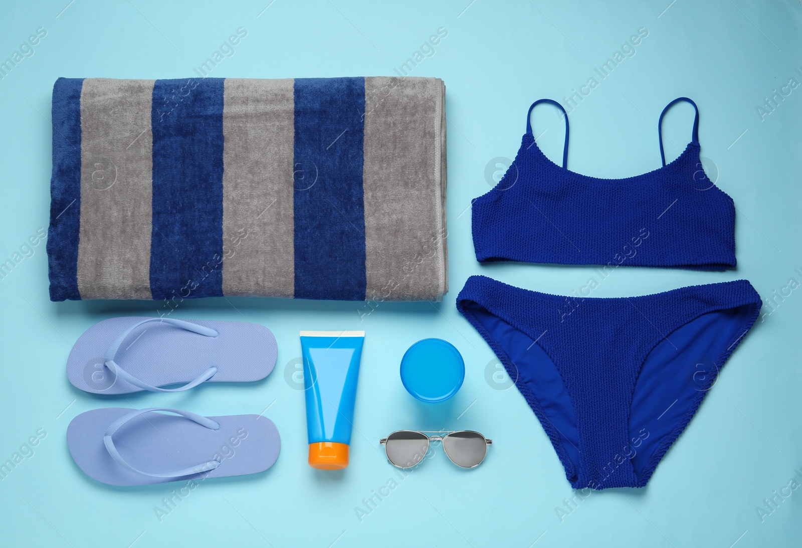 Photo of Beach towel, swimsuit, flip flops, sunglasses and sun protection product on light blue background, flat lay