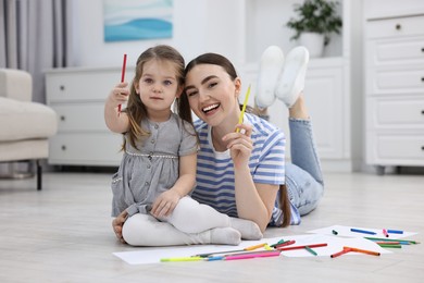 Photo of Mother and her little daughter drawing with colorful markers on floor at home