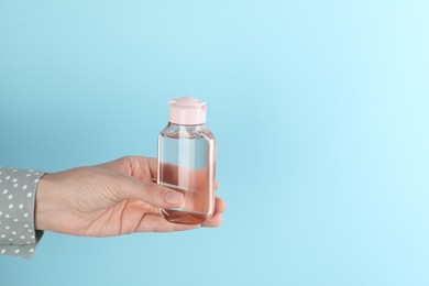 Woman holding micellar water in bottle on light blue background, space for text