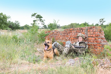 Man in military uniform with German shepherd dog near broken brick wall