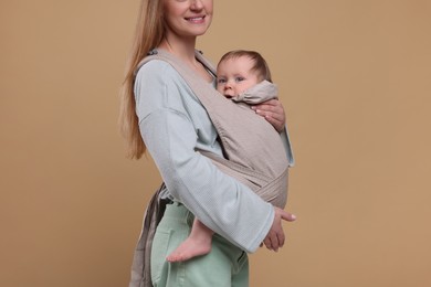 Photo of Mother holding her child in sling (baby carrier) on light brown background, closeup