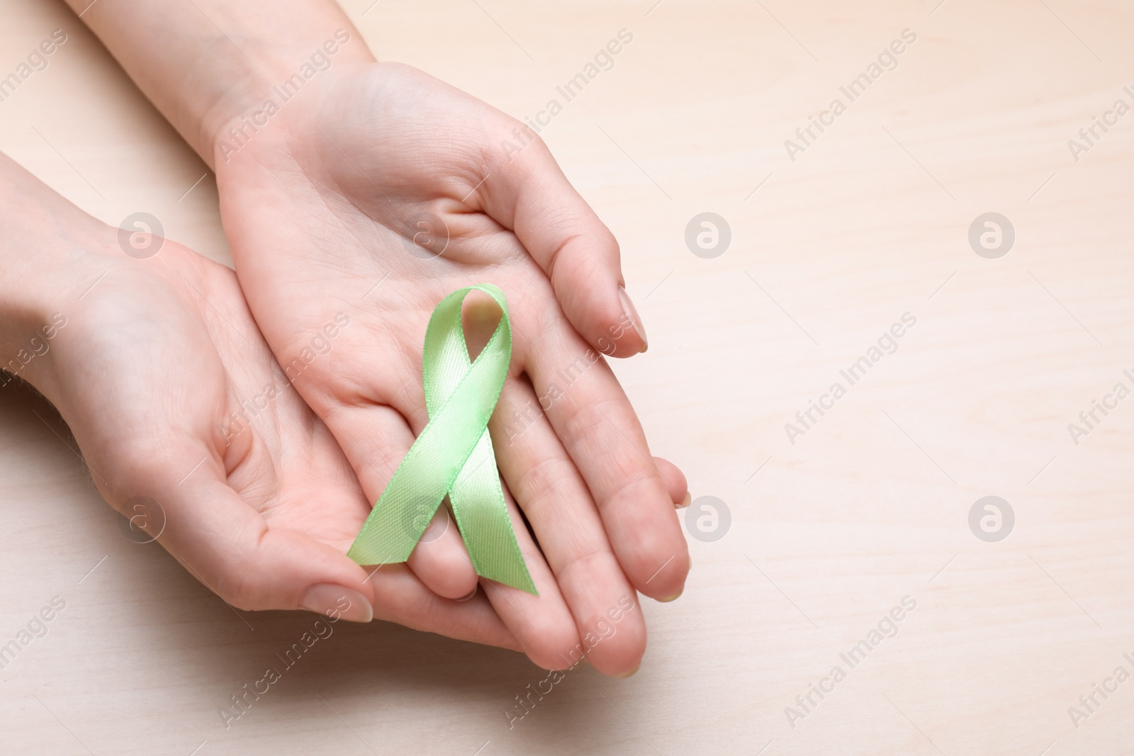 Photo of World Mental Health Day. Woman holding green ribbon on wooden background, top view with space for text