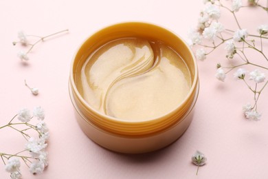 Under eye patches in jar and flowers on light pink background, closeup. Cosmetic product