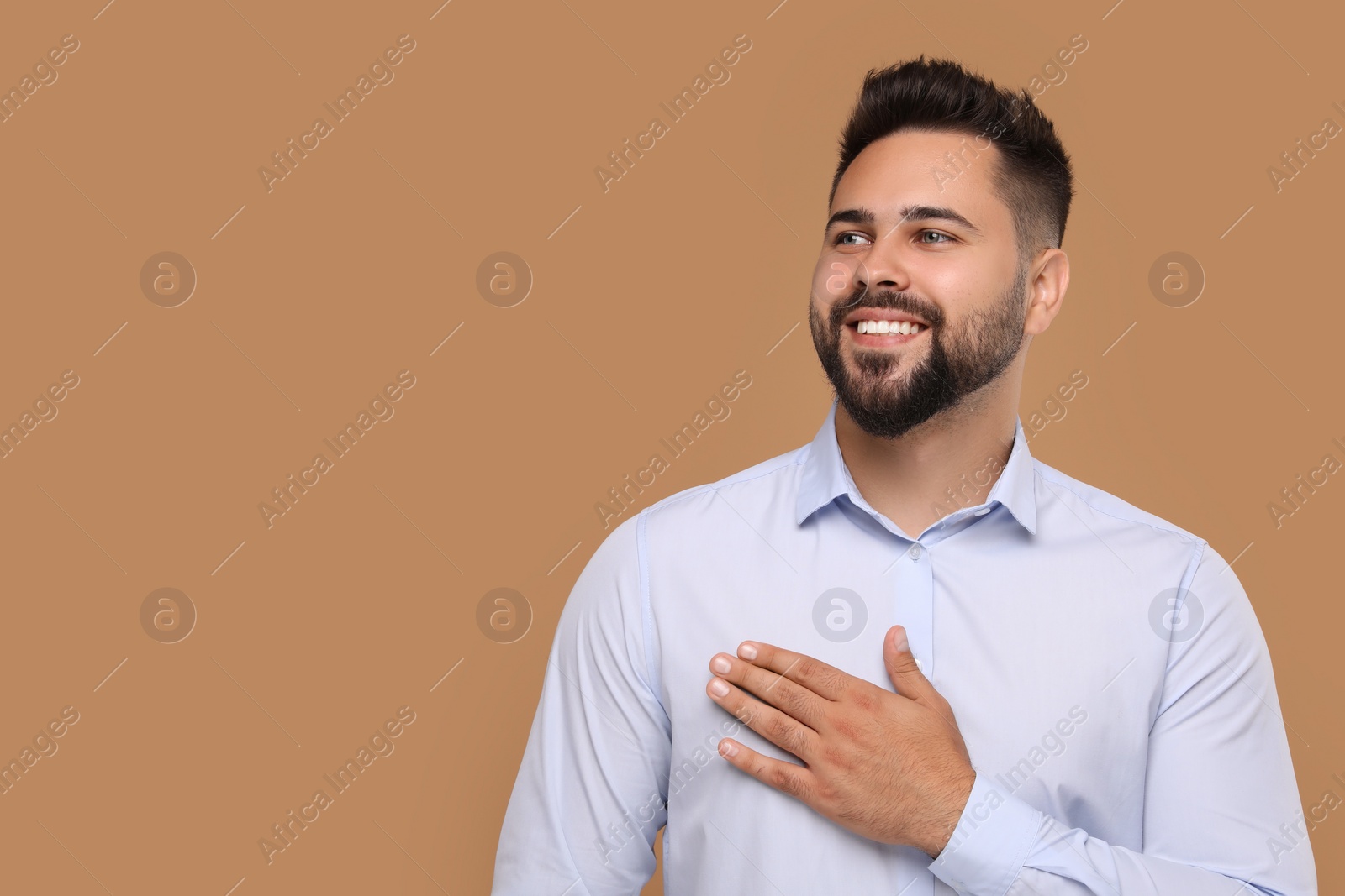 Photo of Thank you gesture. Handsome grateful man holding hand near heart on brown background, space for text