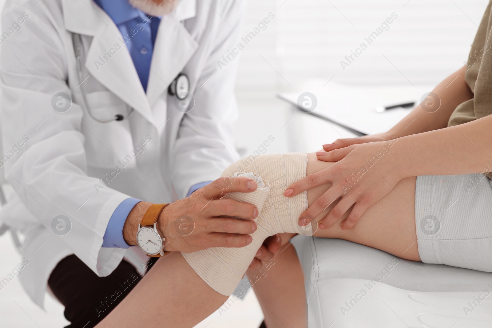 Photo of Orthopedist applying bandage onto patient's knee in clinic, closeup