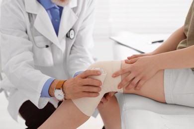 Orthopedist applying bandage onto patient's knee in clinic, closeup