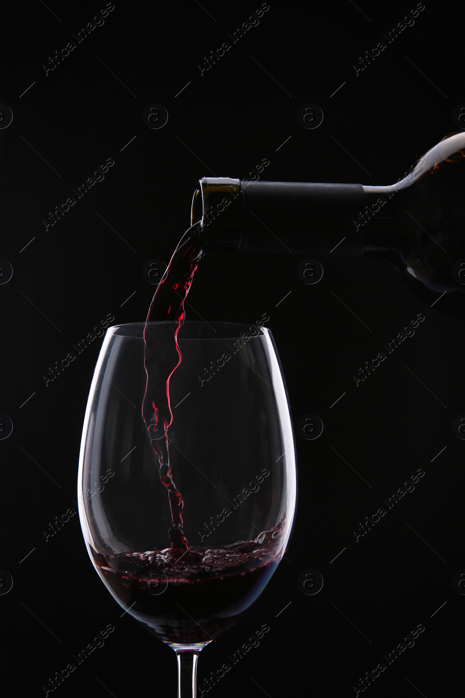 Photo of Pouring red wine from bottle into glass on black background, closeup