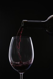 Photo of Pouring red wine from bottle into glass on black background, closeup