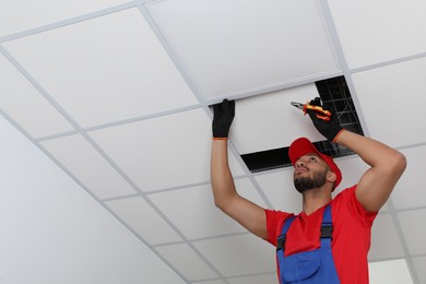Electrician with pliers repairing ceiling light indoors, low angle view. Space for text