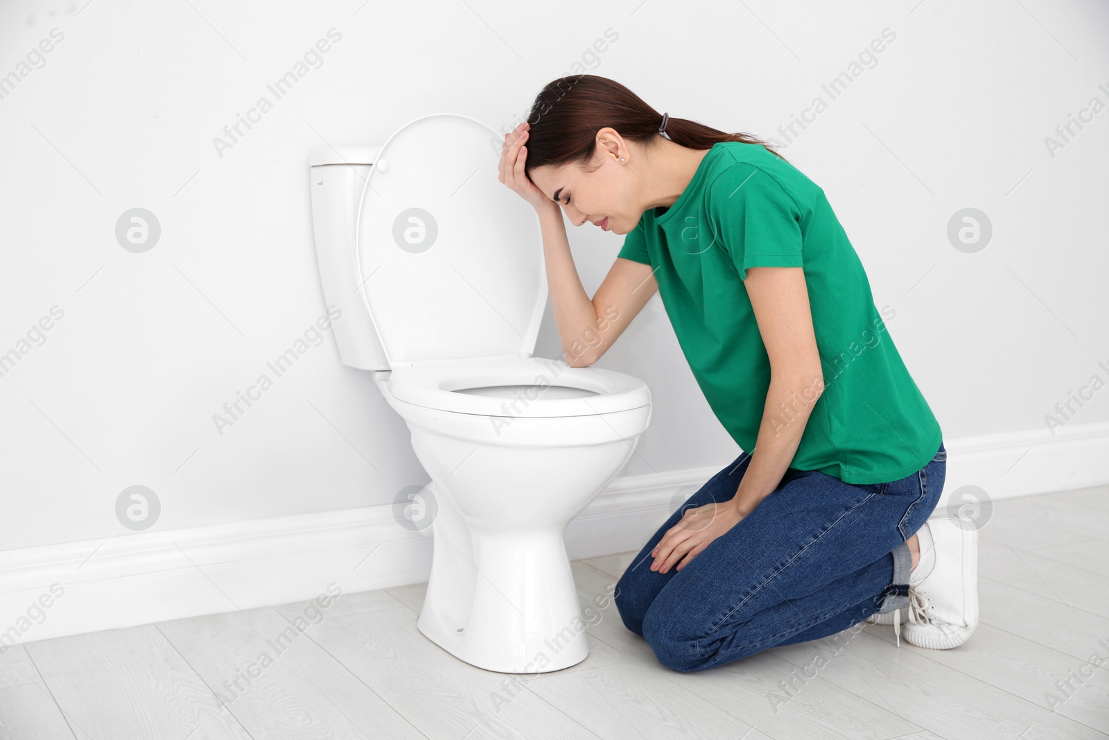 Photo of Young woman suffering from nausea at toilet bowl indoors. Space for text