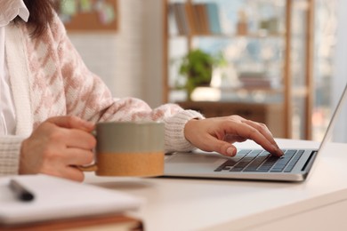 Photo of Woman with modern laptop and cup of tea learning at home, closeup