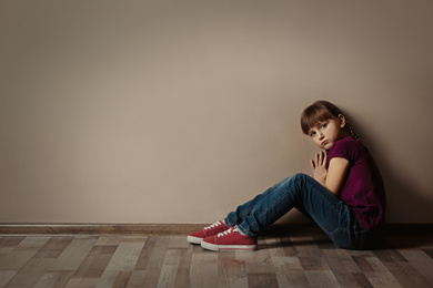 Sad little girl sitting on floor indoors, space for text. Child in danger
