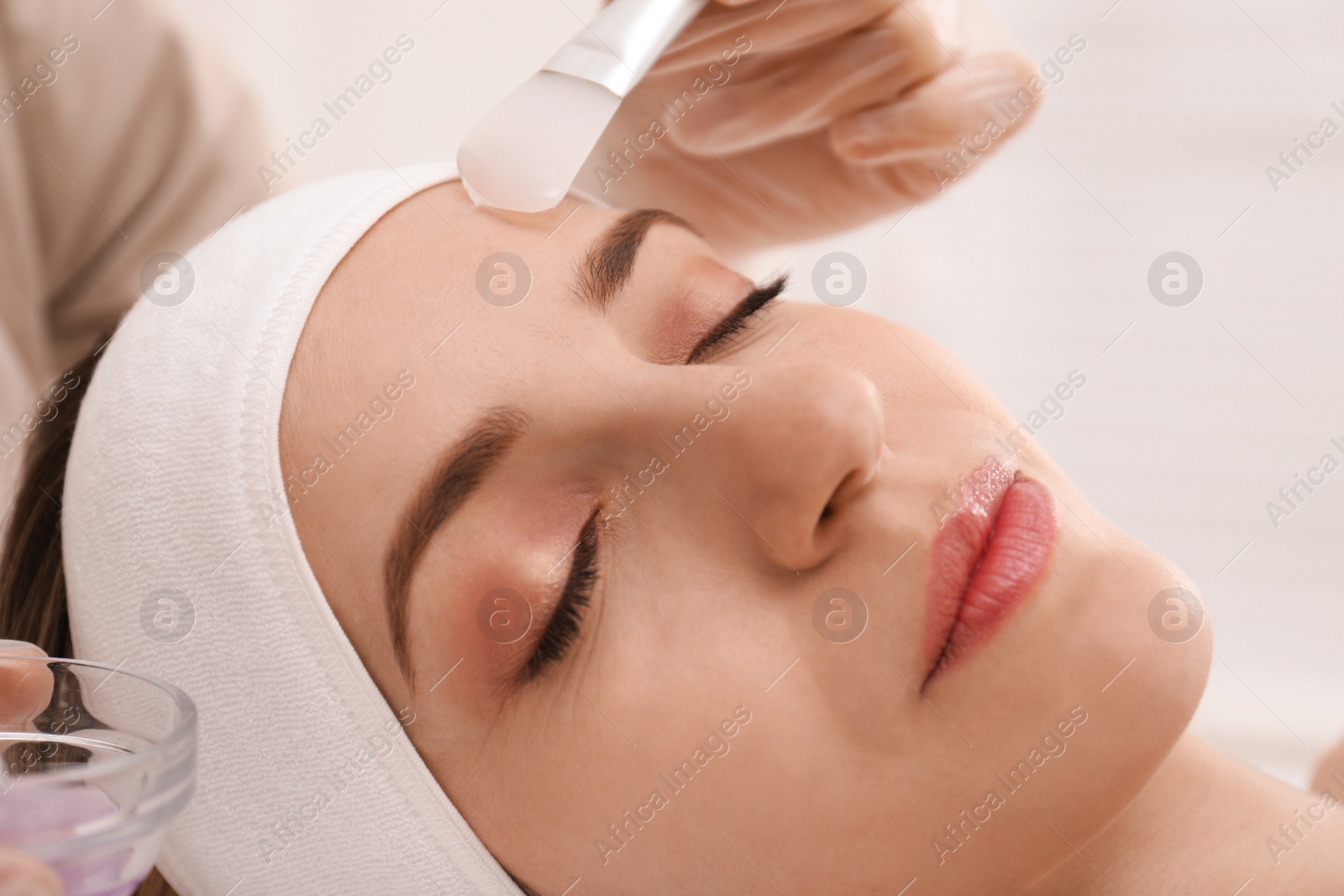 Photo of Young woman during face peeling procedure in salon, closeup