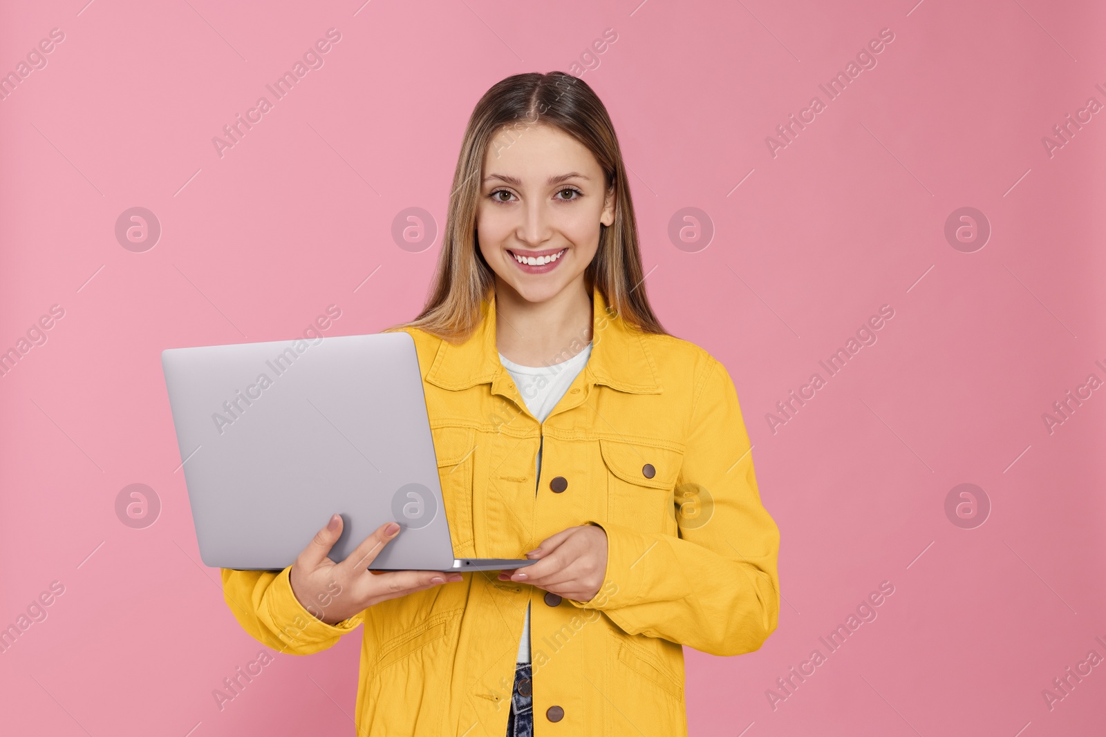 Photo of Beautiful teenage girl using laptop on pink background