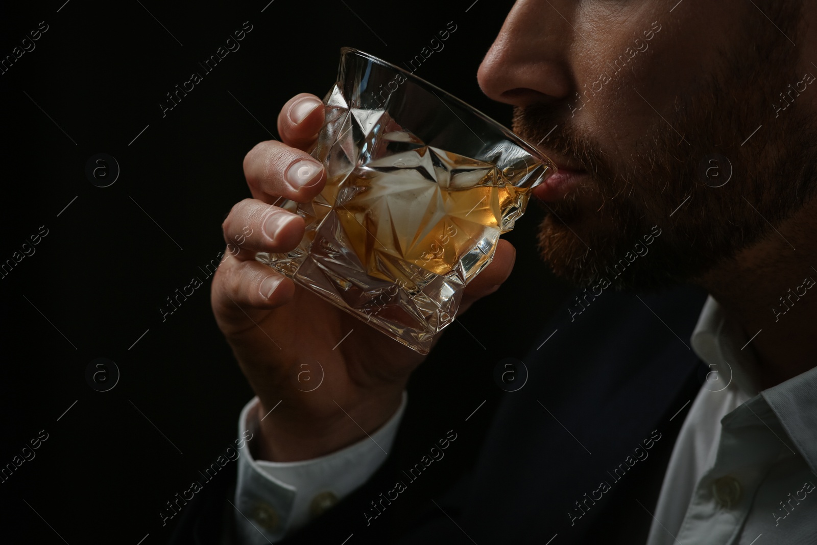 Photo of Man in suit drinking whiskey on black background, closeup