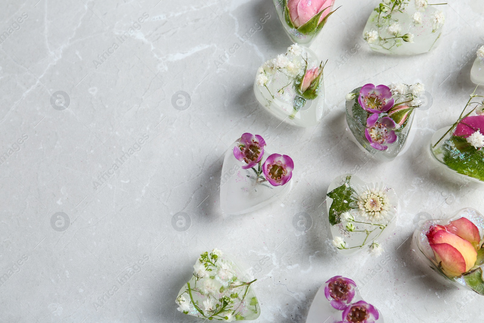 Photo of Heart shaped ice cubes with flowers on grey background, flat lay. Space for text