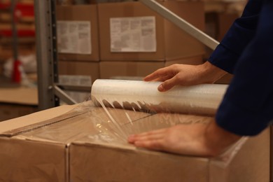 Worker wrapping boxes in stretch film at warehouse, closeup