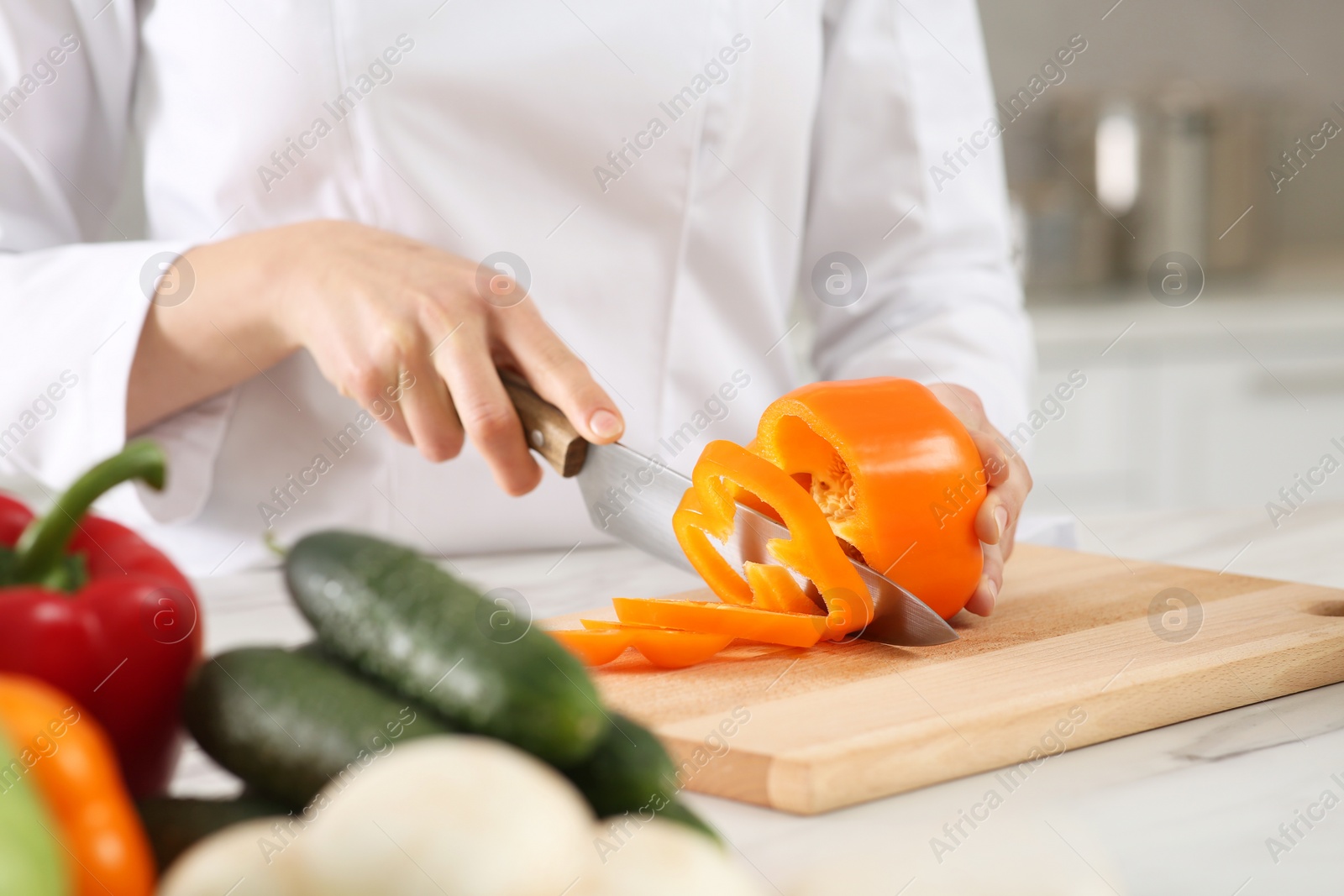 Photo of Professional chef cutting cut bell pepper at white marble table in kitchen, closeup