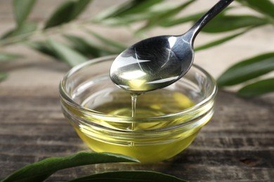 Photo of Pouring olive oil from spoon into glass bowl on wooden table, closeup