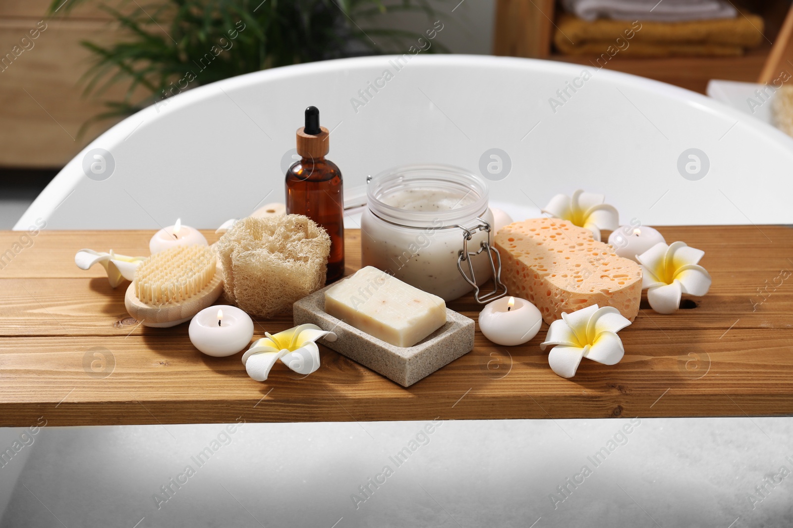 Photo of Composition with different spa products and beautiful flowers on tub tray in bathroom