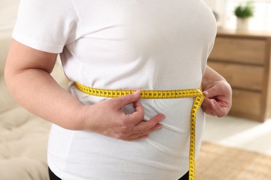 Overweight woman measuring waist with tape at home, closeup