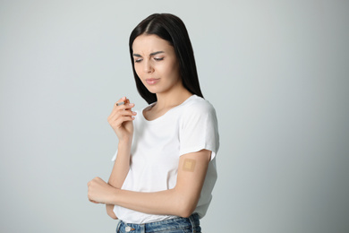 Photo of Emotional young woman with nicotine patch and cigarette on light grey background