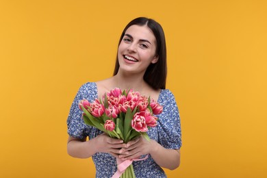 Photo of Happy young woman with beautiful bouquet on orange background