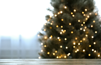 Photo of Blurred view of beautiful Christmas tree with yellow lights near window indoors, focus on wooden table. Space for text