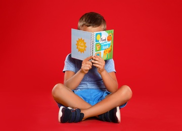 Photo of Cute little boy reading book on red background