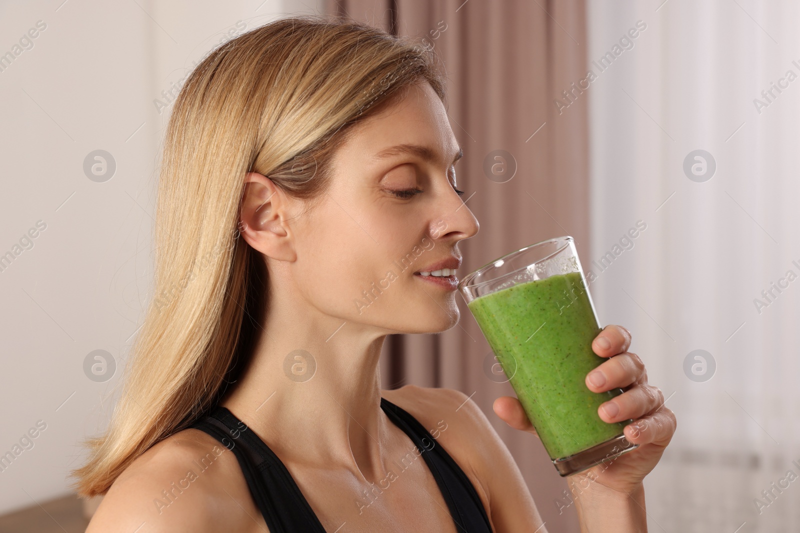 Photo of Young woman in sportswear with glass of fresh smoothie at home