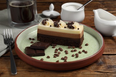 Plate with tasty mousse cake, chocolate and fork on wooden table