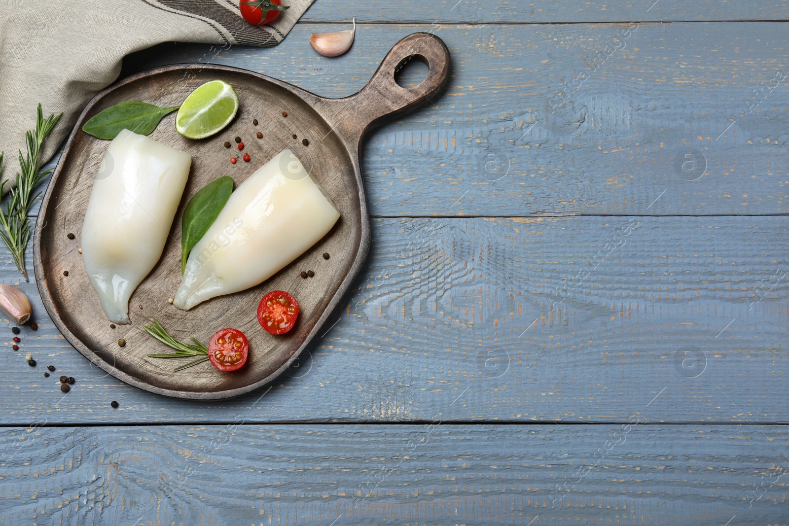 Photo of Flat lay composition with fresh raw squid tubes and garnish ingredients on grey wooden table. Space for text